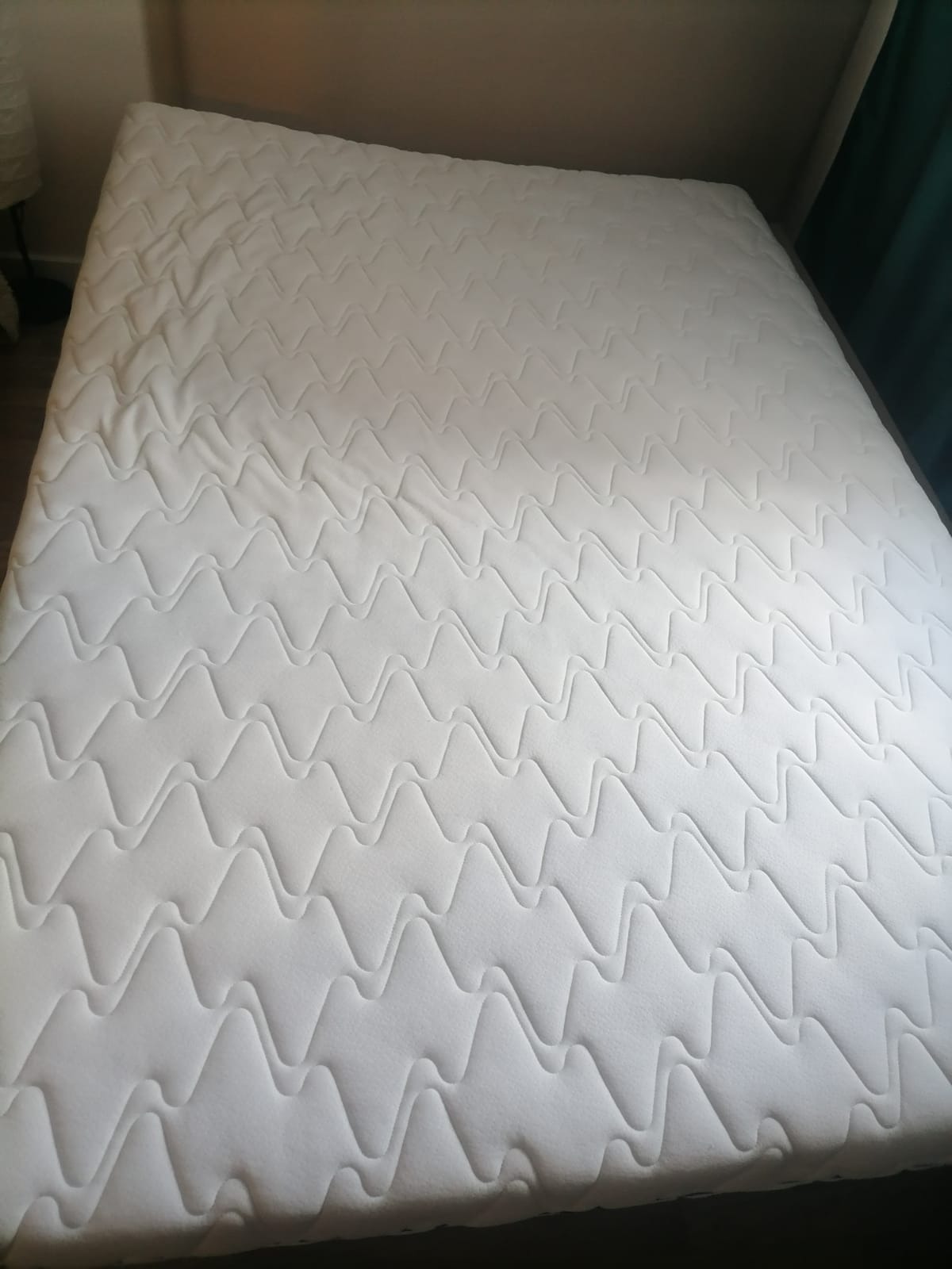 Czysty, biały materac z charakterystycznym, zygzakowatym wzorem pikowania na powierzchni, leżący na łóżku.
