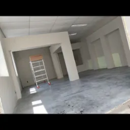 Wnętrze biura w trakcie remontu z zamontowanymi płytami na ścianach i suficie, widoczna aluminiowa drabina na kółkach.