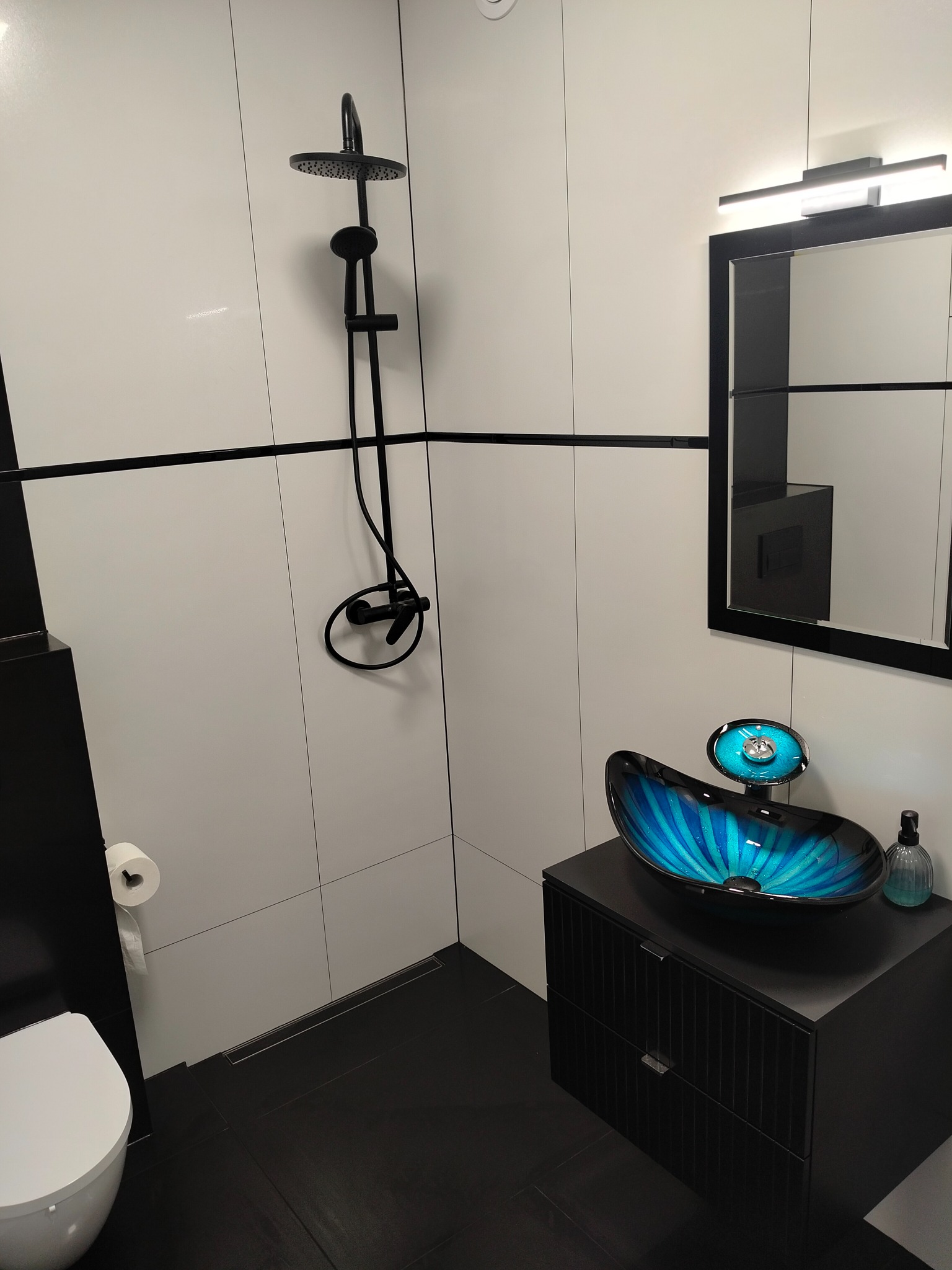 Nowoczesna łazienka z czarno-białymi płytkami, czarną armaturą i umywalką w kolorze turkusowym. Minimalistyczny design z akcentem kolorystycznym.