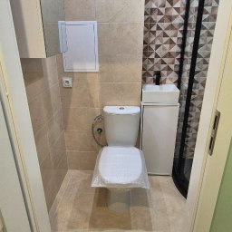 My House - Wykończona łazienka w beżach z akcentem geometrycznych płytek. Umywalka z szafką, toaleta z zabezpieczeniem, kabina prysznicowa z czarnymi ramami.
