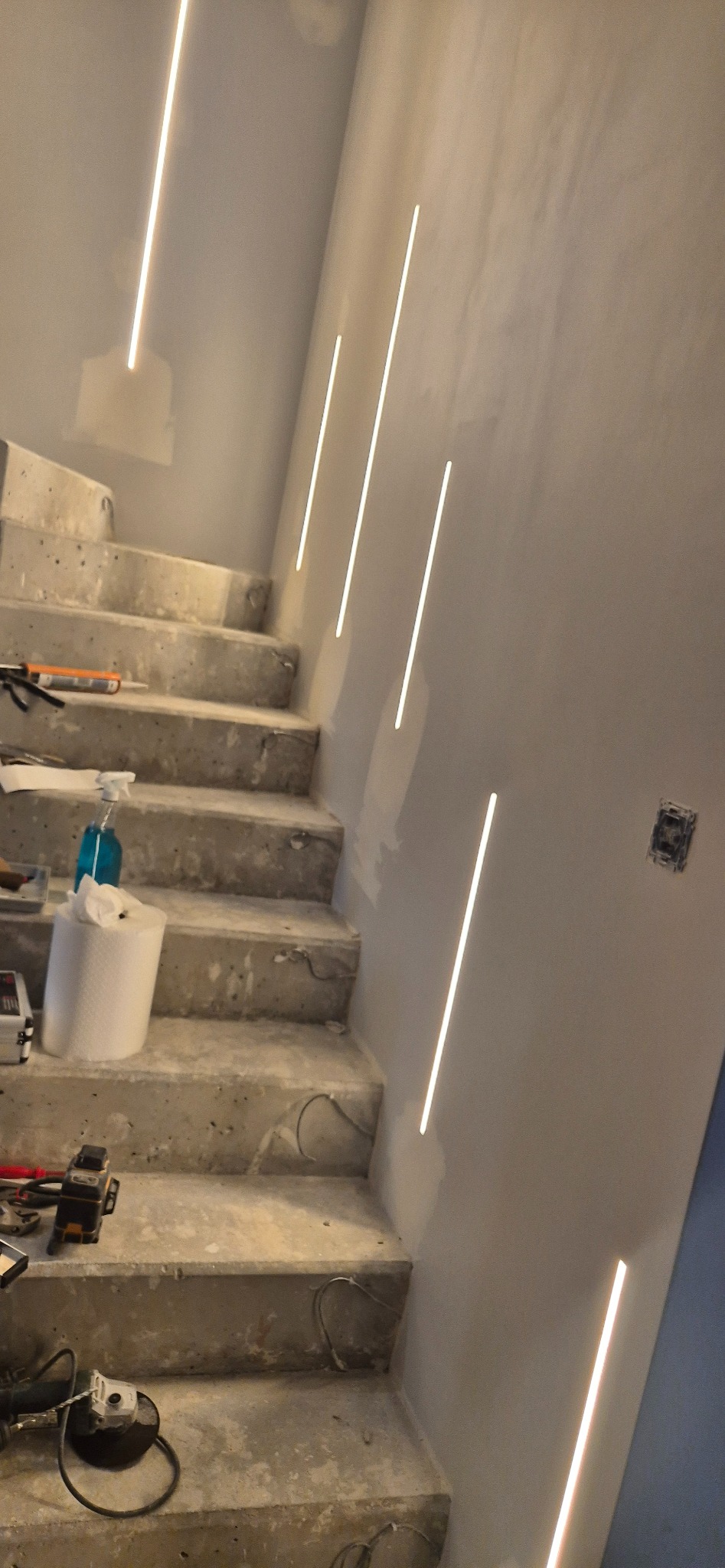 Betonowe schody z zamontowanym oświetleniem liniowym w ścianie. Widoczne narzędzia i materiały budowlane. Etap wykończenia wnętrza.