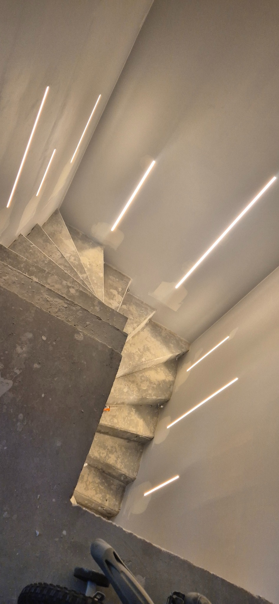 Surowe schody betonowe z liniowym oświetleniem LED wzdłuż ścian i sufitu, widok z góry, etap wykończenia wnętrza, surowy stan.