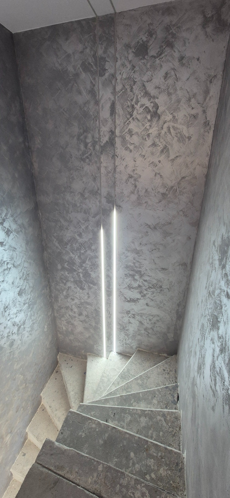 Stylowe wykończenie ścian w Łodzi z efektem betonu architektonicznego, oświetlone pionowymi liniami LED, widok na betonowe schody.