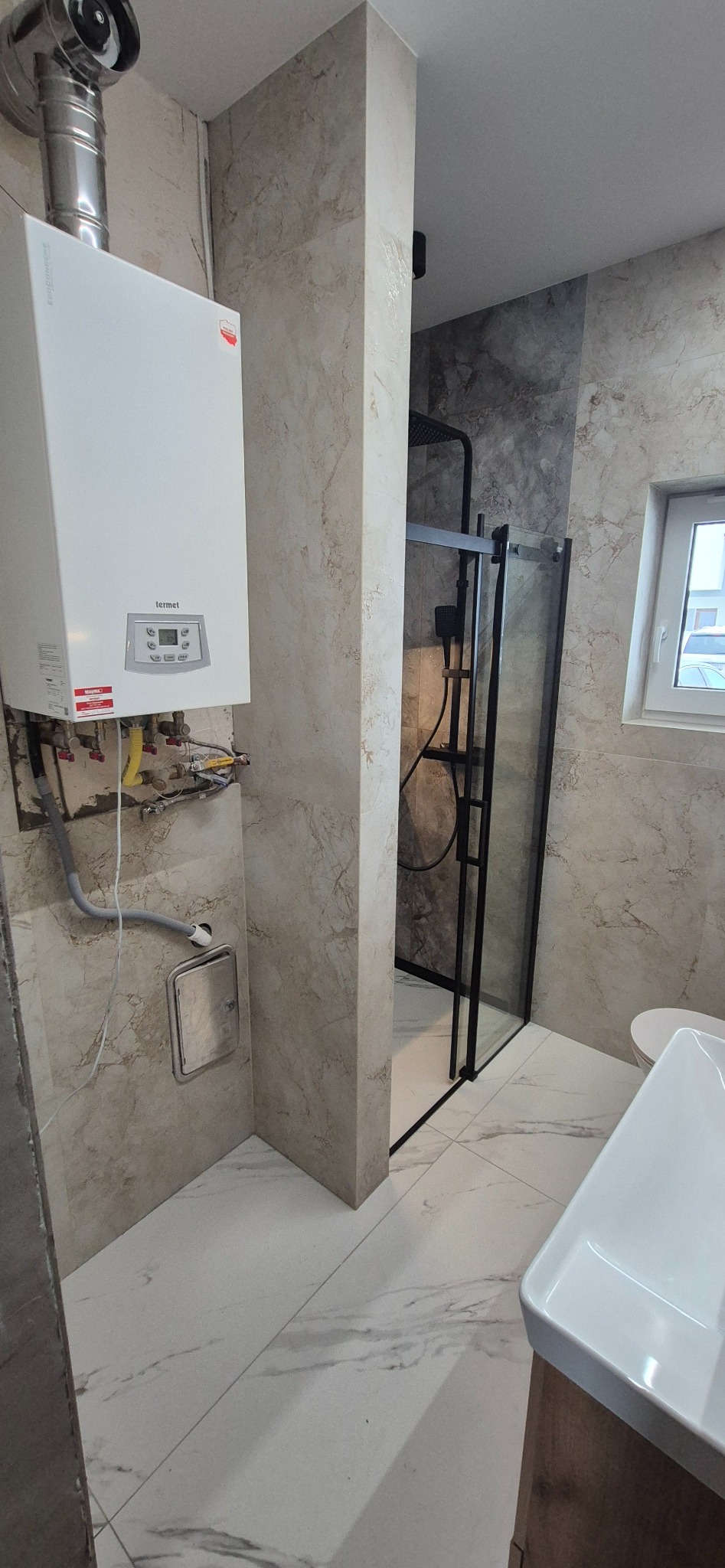 Wykończona łazienka z kabiną prysznicową typu walk-in, marmurowe płytki na ścianach i podłodze, oraz zamontowany piec gazowy Termet. Nowoczesny design.