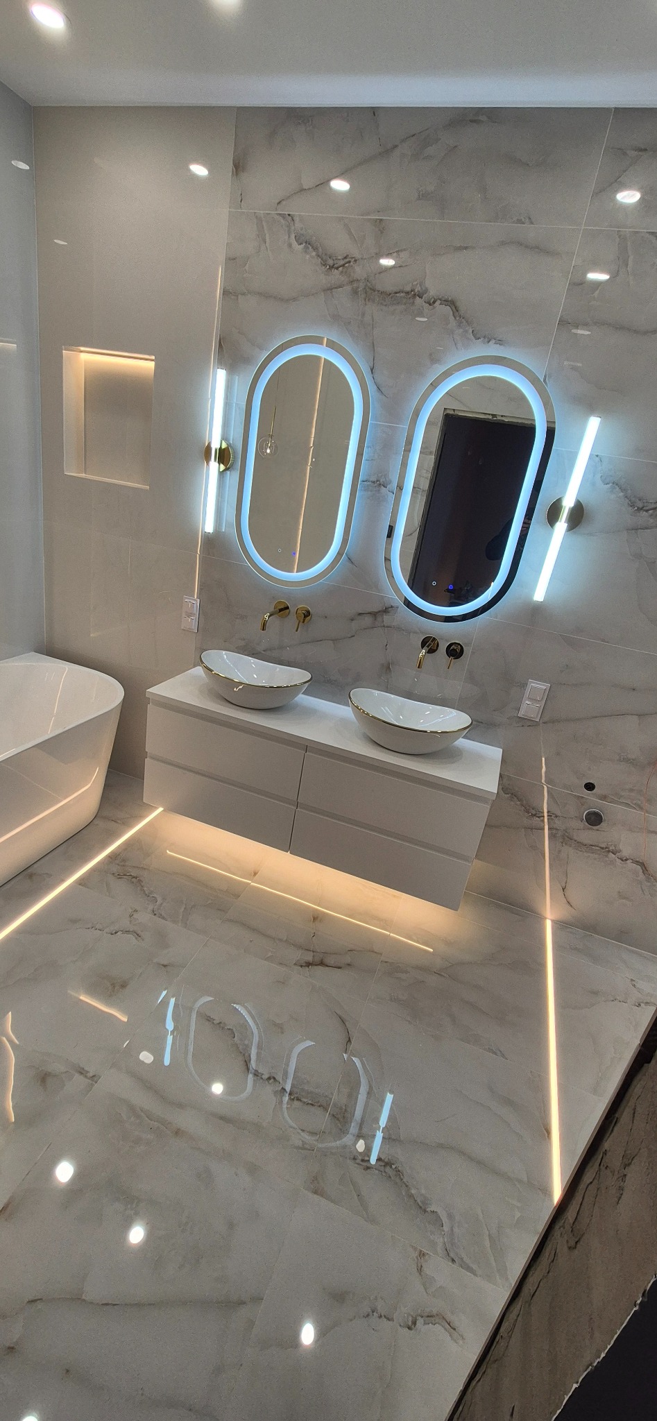 Elegancka łazienka z marmurowymi płytkami, podświetlanymi lustrami i umywalkami w stylu glamour. Nowoczesne wykończenie z dbałością o detale i oświetlenie.