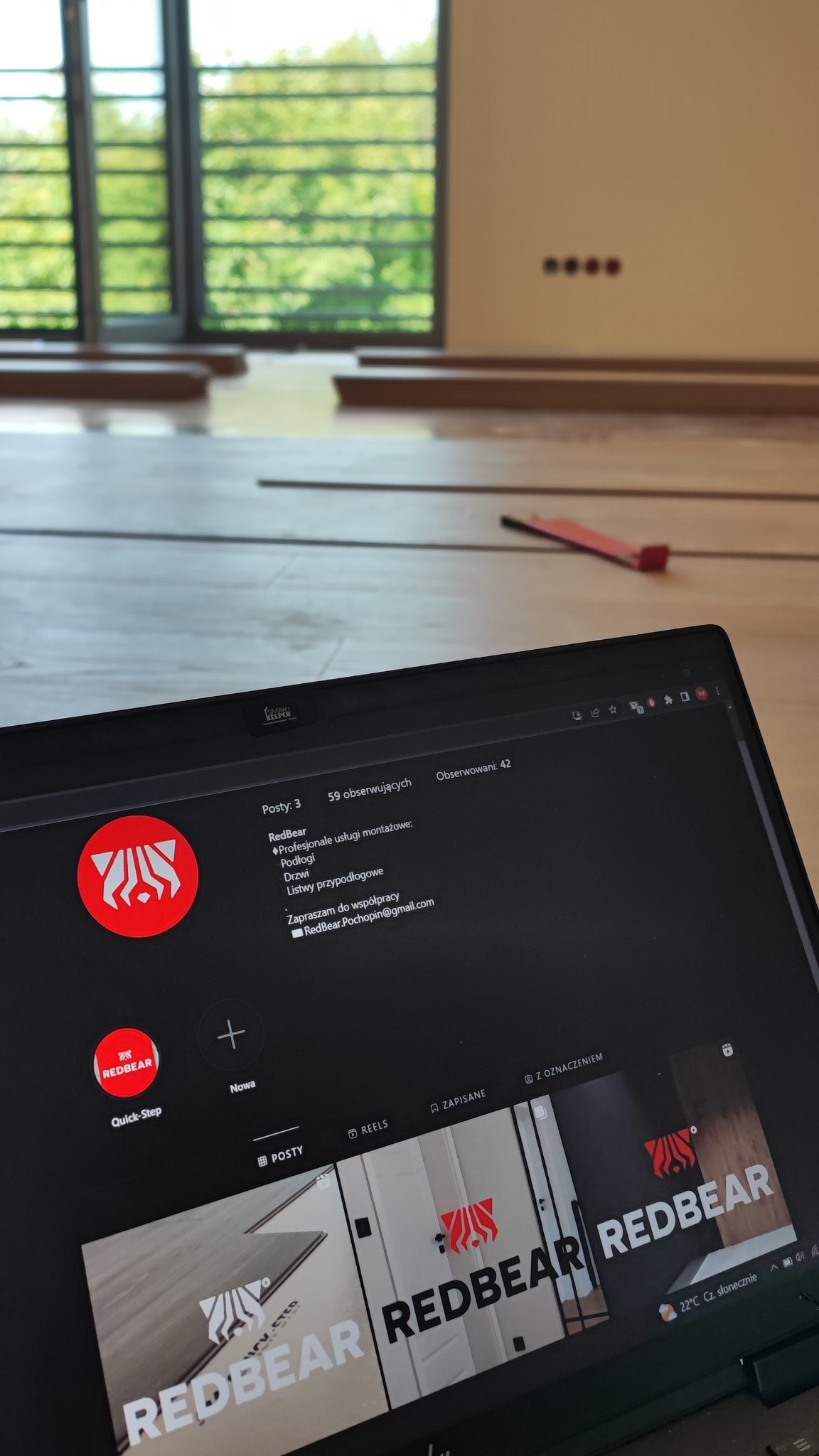Widok na podłogę w trakcie montażu z widocznym laptopem prezentującym profil firmy RedBear, oferującej profesjonalne usługi montażowe podłóg, drzwi i listew przypodłogowych.