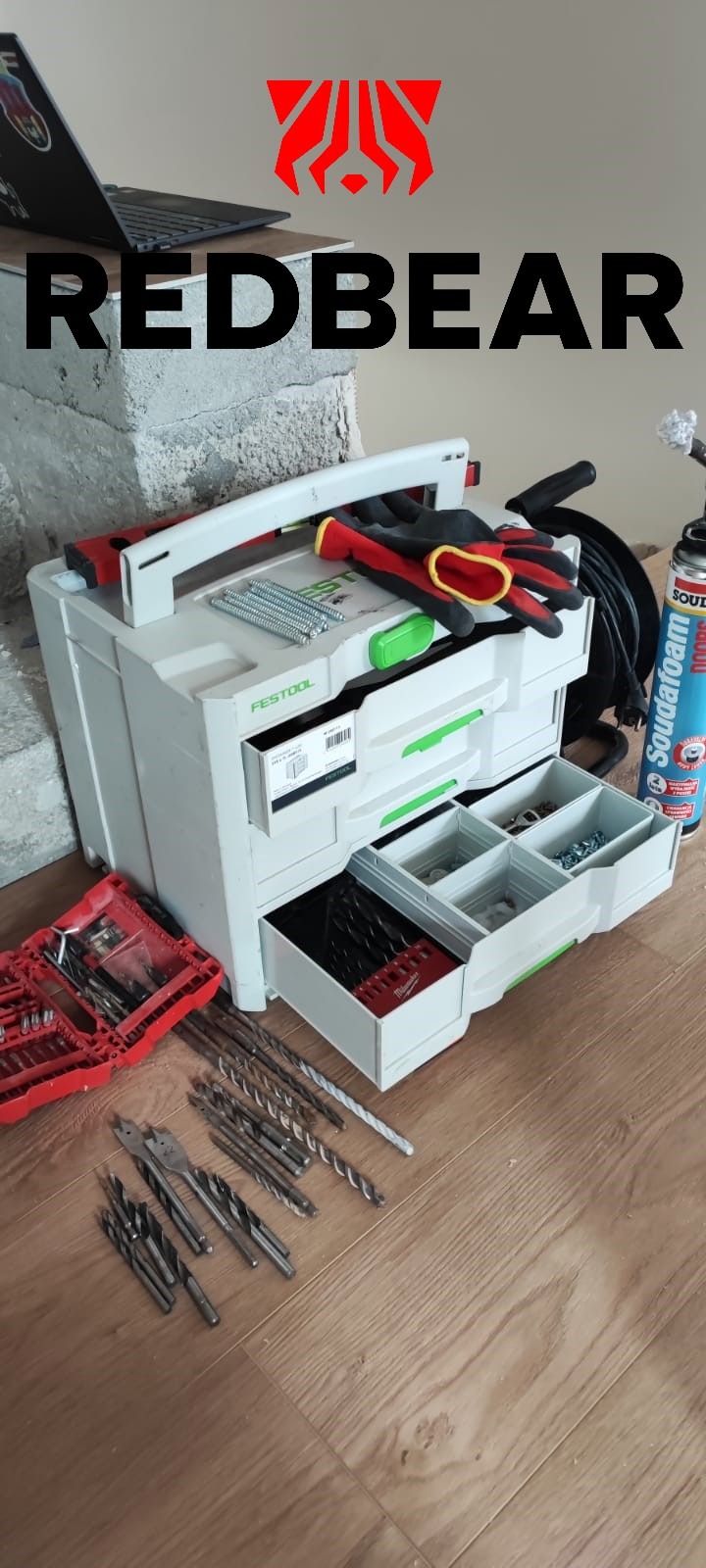 Otwarta skrzynka narzędziowa Festool z wiertłami, wkrętami i rękawicami roboczymi na podłodze z paneli, obok puszka pianki montażowej Soudal.