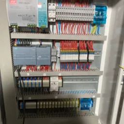 Wnętrze szafy sterowniczej z modułami Siemens, zasilaczami Mean Well, zabezpieczeniami ETI i licznymi połączeniami kablowymi oznaczonymi numerami X1-X7, widoczne również przewody w dolnej części...