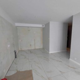 MIKOBUD Mikołaj Krauzowicz - Wnętrze w trakcie prac wykończeniowych: położone marmurowe płytki podłogowe, ściany częściowo przygotowane do malowania, widoczne instalacje.