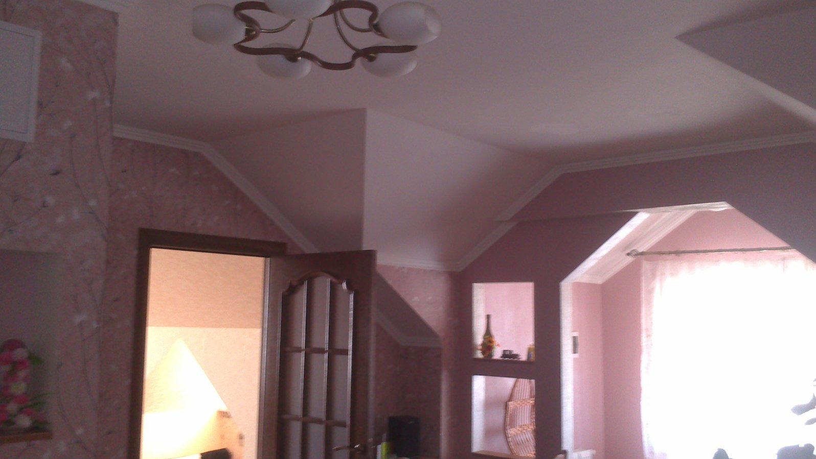 Pokój z różowymi ścianami, dekoracyjną tapetą, białym sufitem ze skosami, sztukaterią i wnękami dekoracyjnymi.