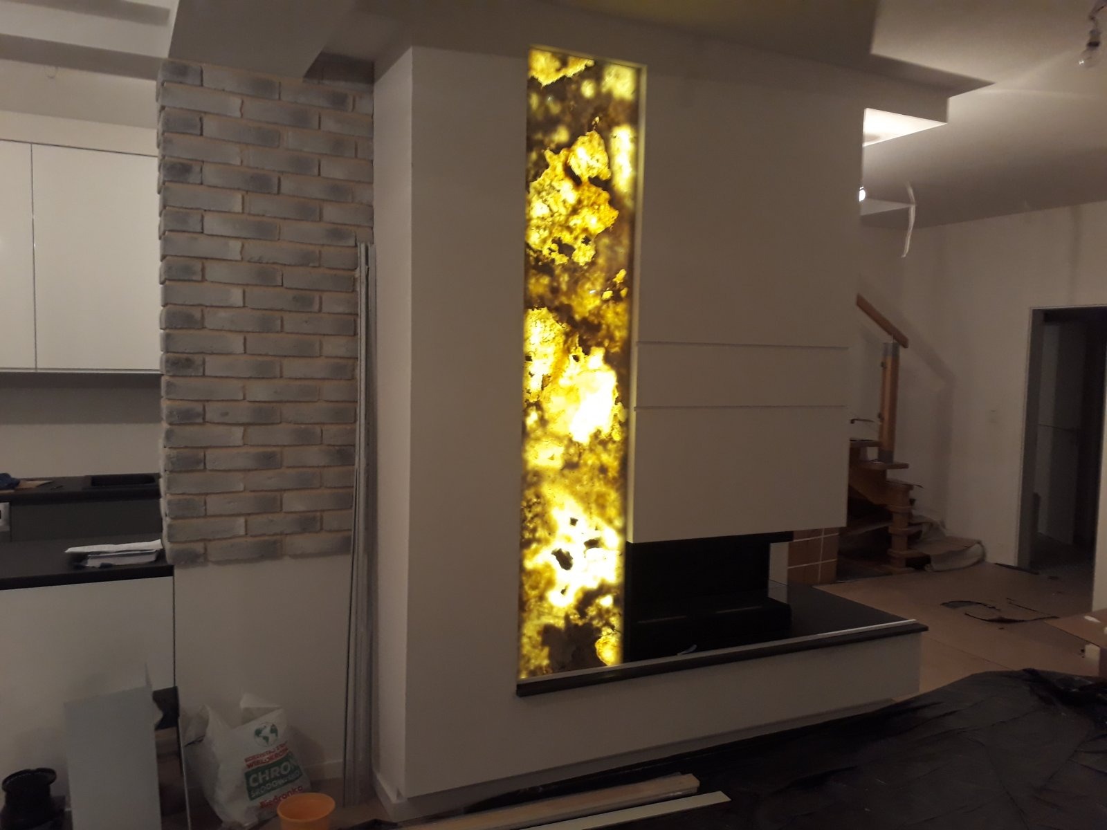 Ściana z wbudowanym podświetlanym panelem z onyksu, obok fragment ściany z cegły dekoracyjnej i widoczna w tle klatka schodowa.