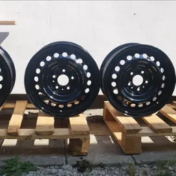 Cztery czarne, stalowe felgi samochodowe z otworami na palecie, po renowacji, z połyskiem, na tle białej ściany i kartonów.