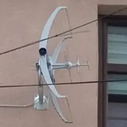 Biała antena paraboliczna zamontowana na elewacji budynku, widoczne kable i okno w tle.