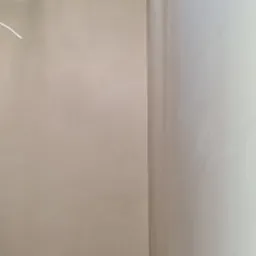 Gładka, jasna ściana po nałożeniu tynku maszynowego, widoczny fragment sufitu z izolacją, surowa podłoga.