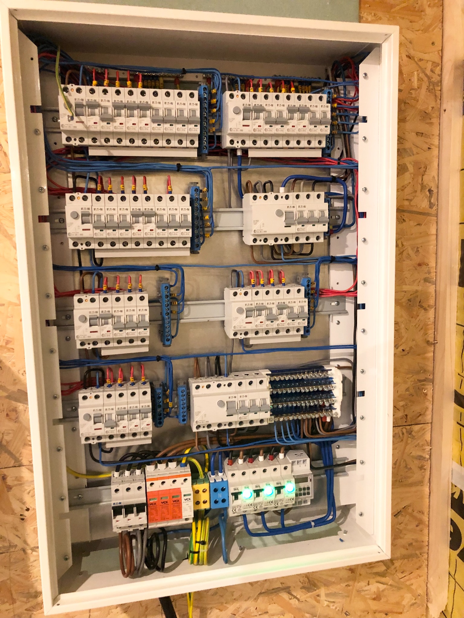 Rozdzielnica elektryczna z zamontowanymi bezpiecznikami, wyłącznikami różnicowoprądowymi i ogranicznikami przepięć, zainstalowana na ścianie z płyty OSB.