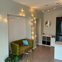 Wnętrze gabinetu z oliwkową sofą, stolikiem z kwiatowym blatem i girlandą świetlną, tworzące przytulną atmosferę.