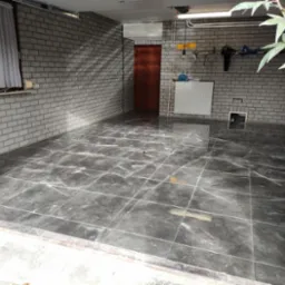 Wyłożona ciemnymi, marmurkowymi płytkami podłoga w pomieszczeniu z ceglanymi ścianami, widoczne narzędzia i roślina w rogu.