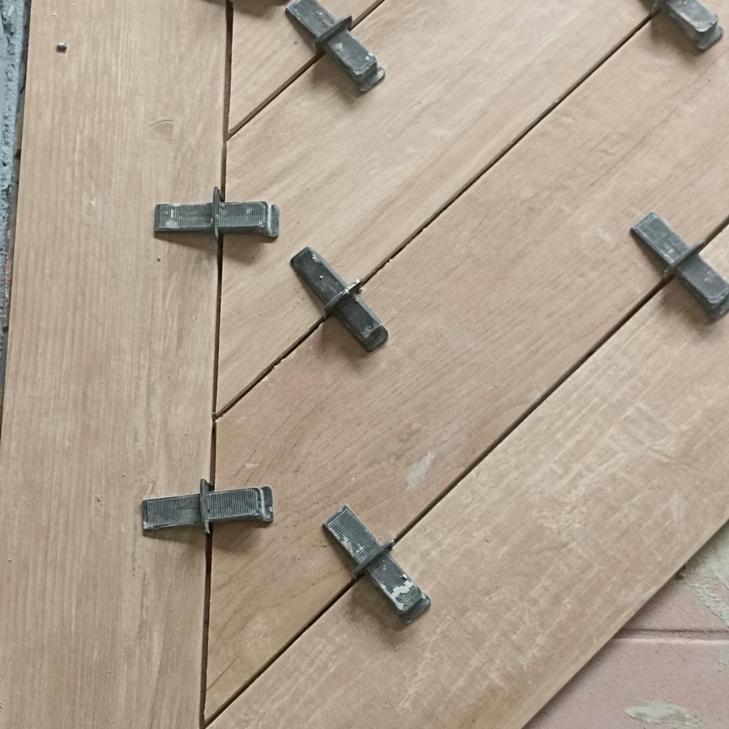 Układanie drewnopodobnych płytek podłogowych w jodełkę, z użyciem klipsów poziomujących, widoczne fragmenty fugi.