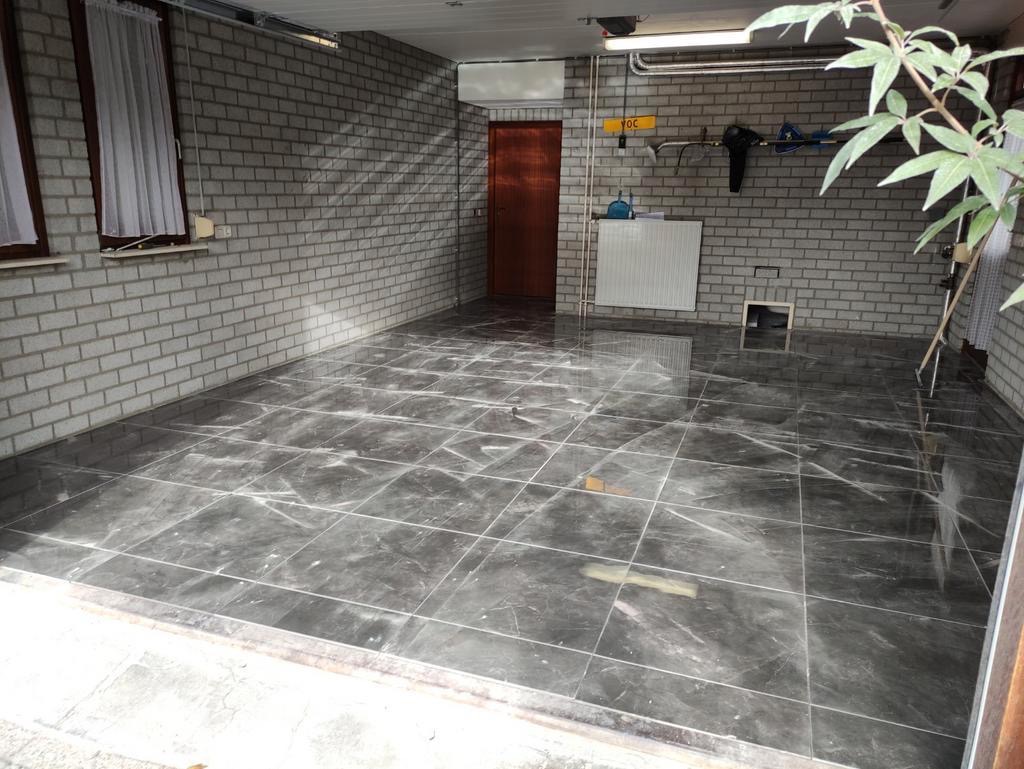 Wyłożona ciemnymi, marmurkowymi płytkami podłoga w pomieszczeniu z ceglanymi ścianami, widoczne narzędzia i roślina w rogu.