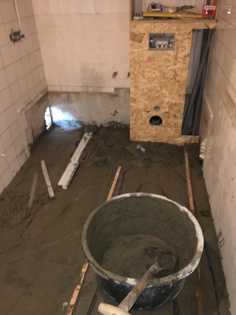 Przygotowanie podłoża pod posadzkę w łazience w Pruszkowie: widoczna wylewka, poziomice oraz wiadro z zaprawą.