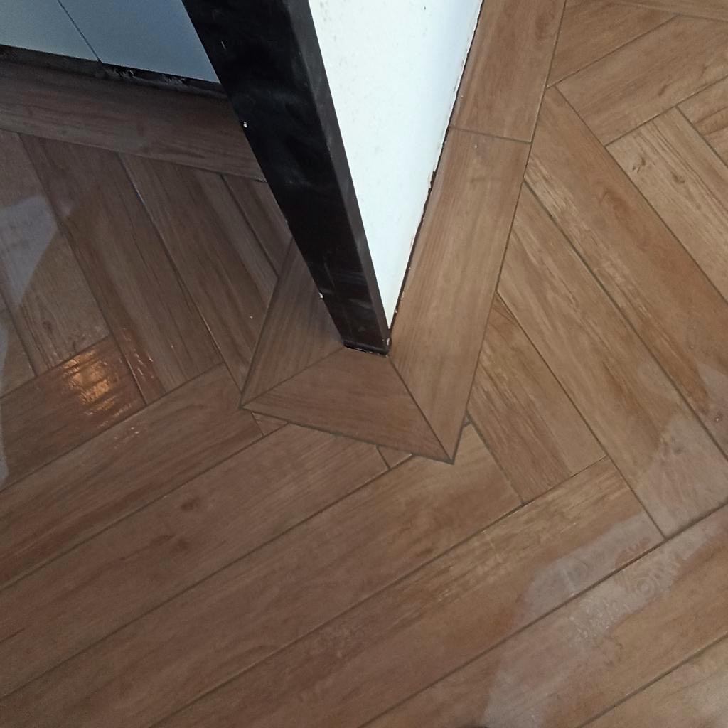 Ułożona w jodełkę podłoga z płytek imitujących drewno, z widocznym progiem i fragmentem ościeżnicy drzwi.