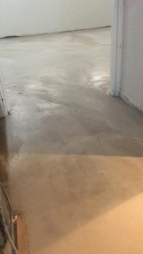 Wylewka samopoziomująca w trakcie schnięcia, widoczne refleksy światła na powierzchni, surowy stan wykończenia wnętrza.