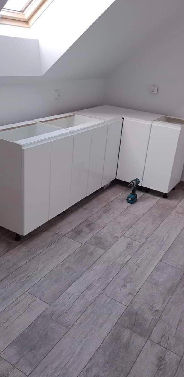 Białe szafki kuchenne bez frontów, zamontowane w skosie poddasza w Białymstoku, z wiertarką akumulatorową leżącą na panelach podłogowych.