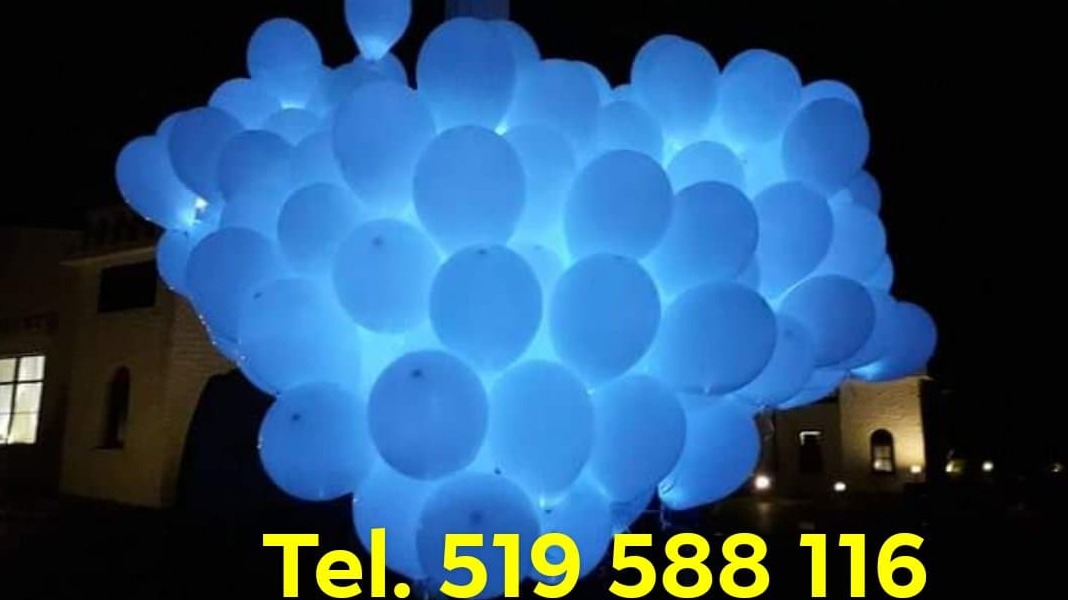 Duża wiązka białych balonów z niebieskim podświetleniem LED, widoczny numer telefonu, budynek w tle, noc.