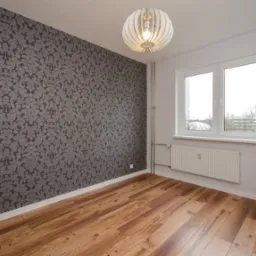 Pokój po odświeżeniu: ściana z szarą tapetą w ornamenty, drewniana podłoga, białe okno z widokiem na zewnątrz i designerska lampa wisząca.