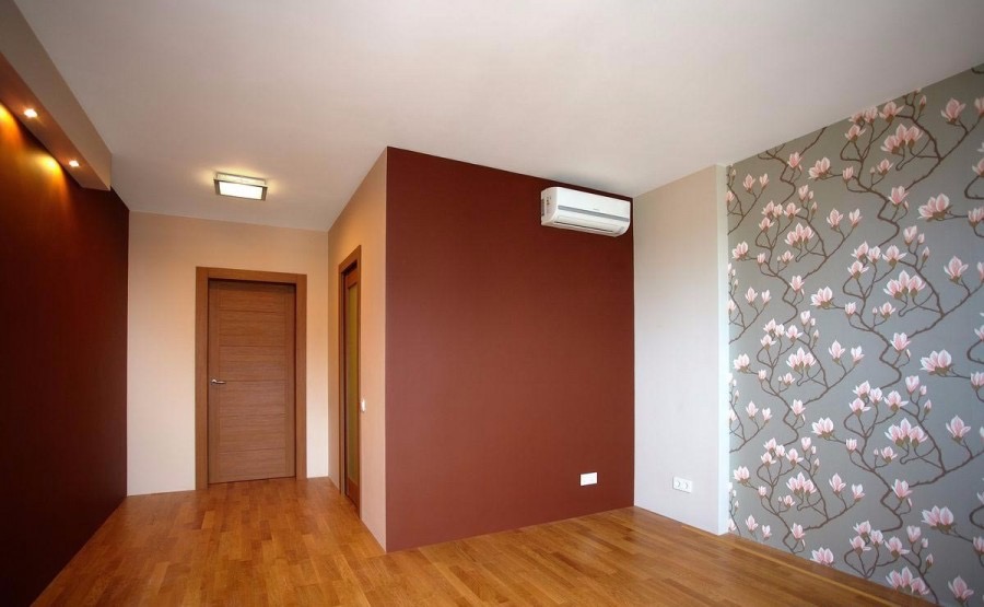 Wnętrze pokoju po remoncie z drewnianą podłogą, brązową ścianą, ścianą z tapetą w kwiaty magnolii i zamontowanym klimatyzatorem.