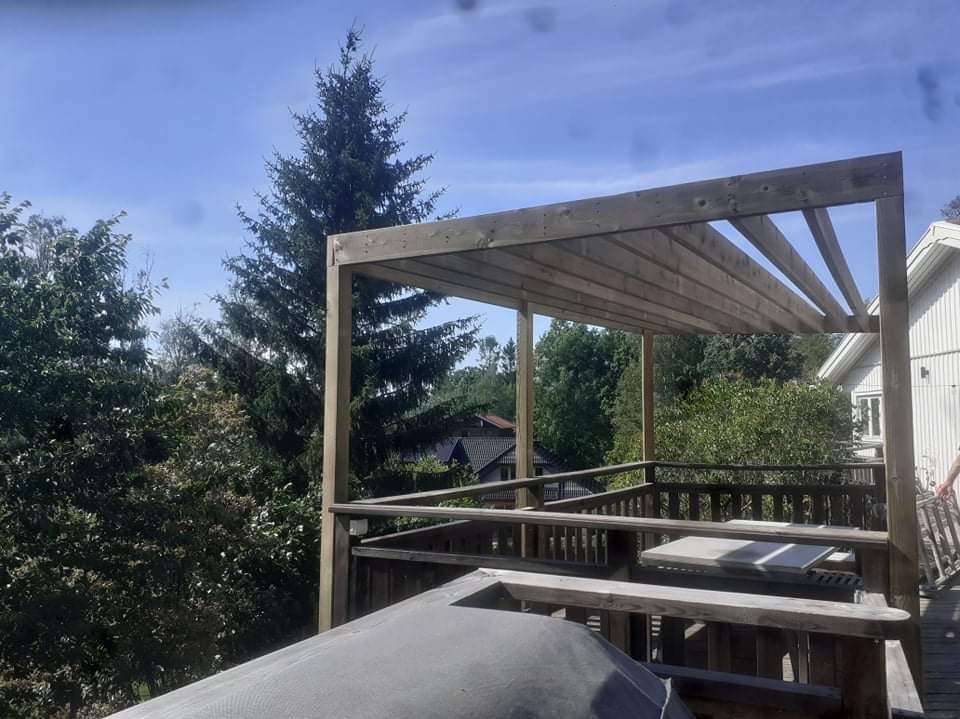 Drewniana pergola zadaszająca taras, widok na zieleń i błękitne niebo, konstrukcja z surowego drewna.