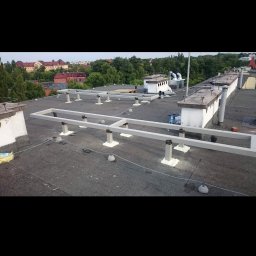 Brak - Montaż stelaża pod instalację na płaskim dachu budynku, widoczne elementy konstrukcyjne i uszczelnienia, w tle zabudowa miejska.