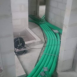 Brak - Zielone, karbowane rury wentylacyjne ułożone w korytarzu w trakcie instalacji w surowym wnętrzu budynku z pustaków.