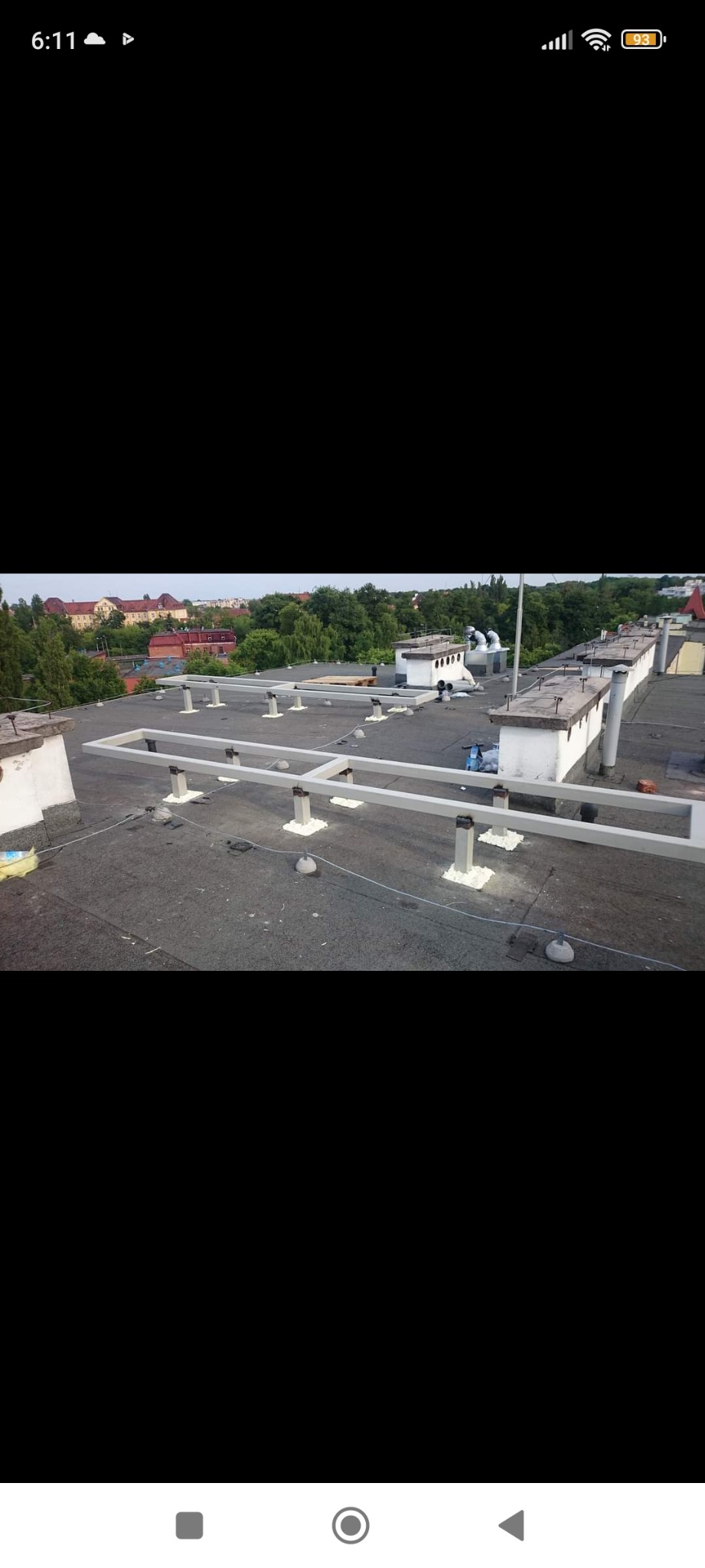 Montaż stelaża pod instalację na płaskim dachu budynku, widoczne elementy konstrukcyjne i uszczelnienia, w tle zabudowa miejska.