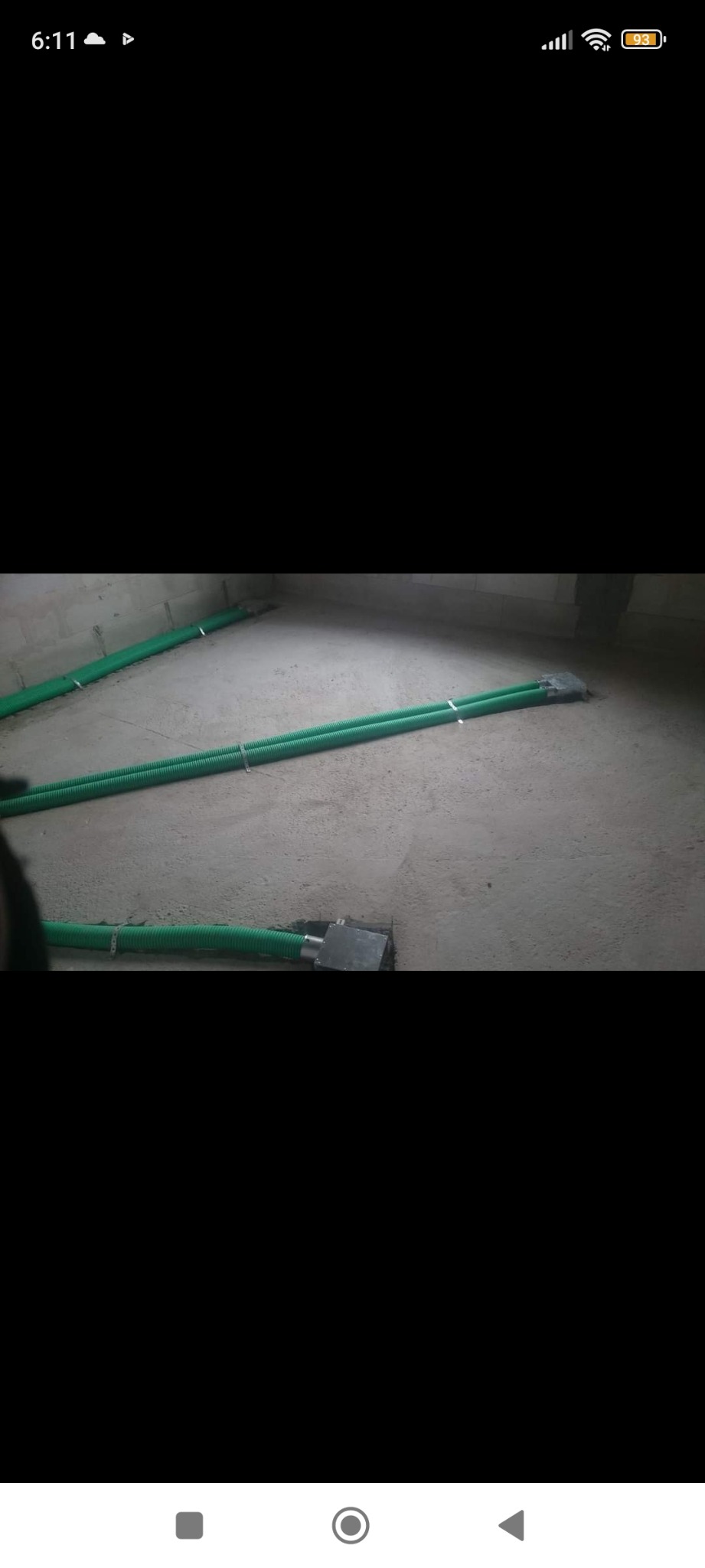 Zielone, karbowane rury wentylacyjne przymocowane metalowymi obejmami do surowego betonowego podłoża w trakcie instalacji systemu wentylacji w pomieszczeniu.