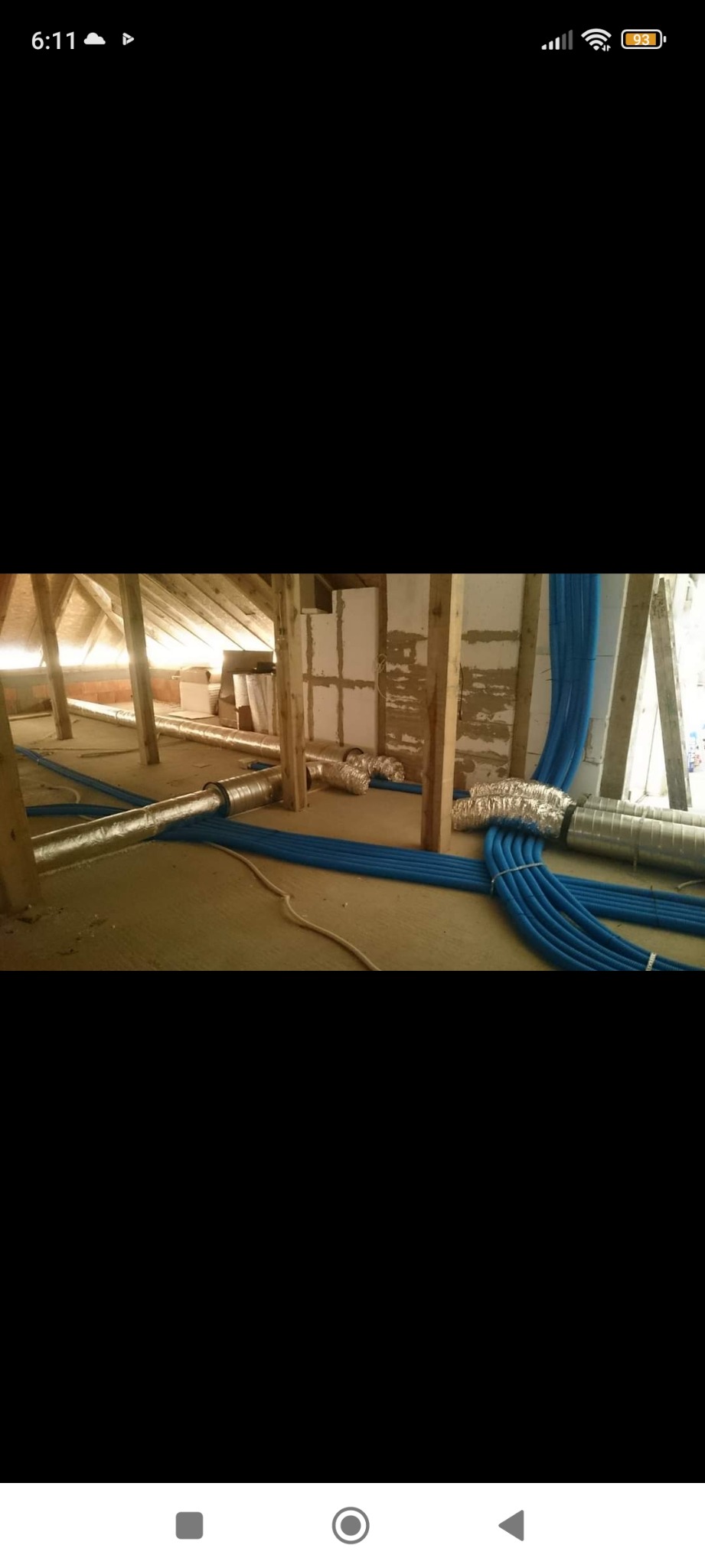 Instalacja przewodów wentylacyjnych i niebieskich rur w surowym wnętrzu poddasza z drewnianą konstrukcją, widoczne fragmenty ocieplonych ścian.