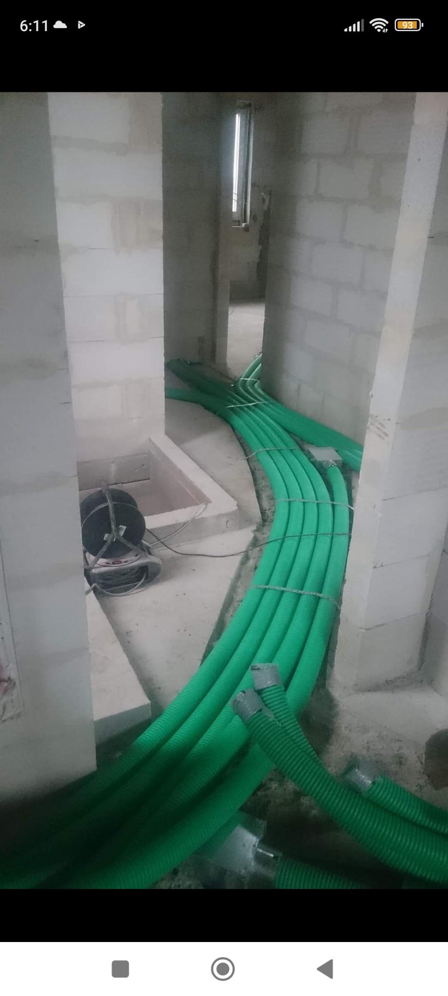 Zielone, karbowane rury wentylacyjne ułożone w korytarzu w trakcie instalacji w surowym wnętrzu budynku z pustaków.