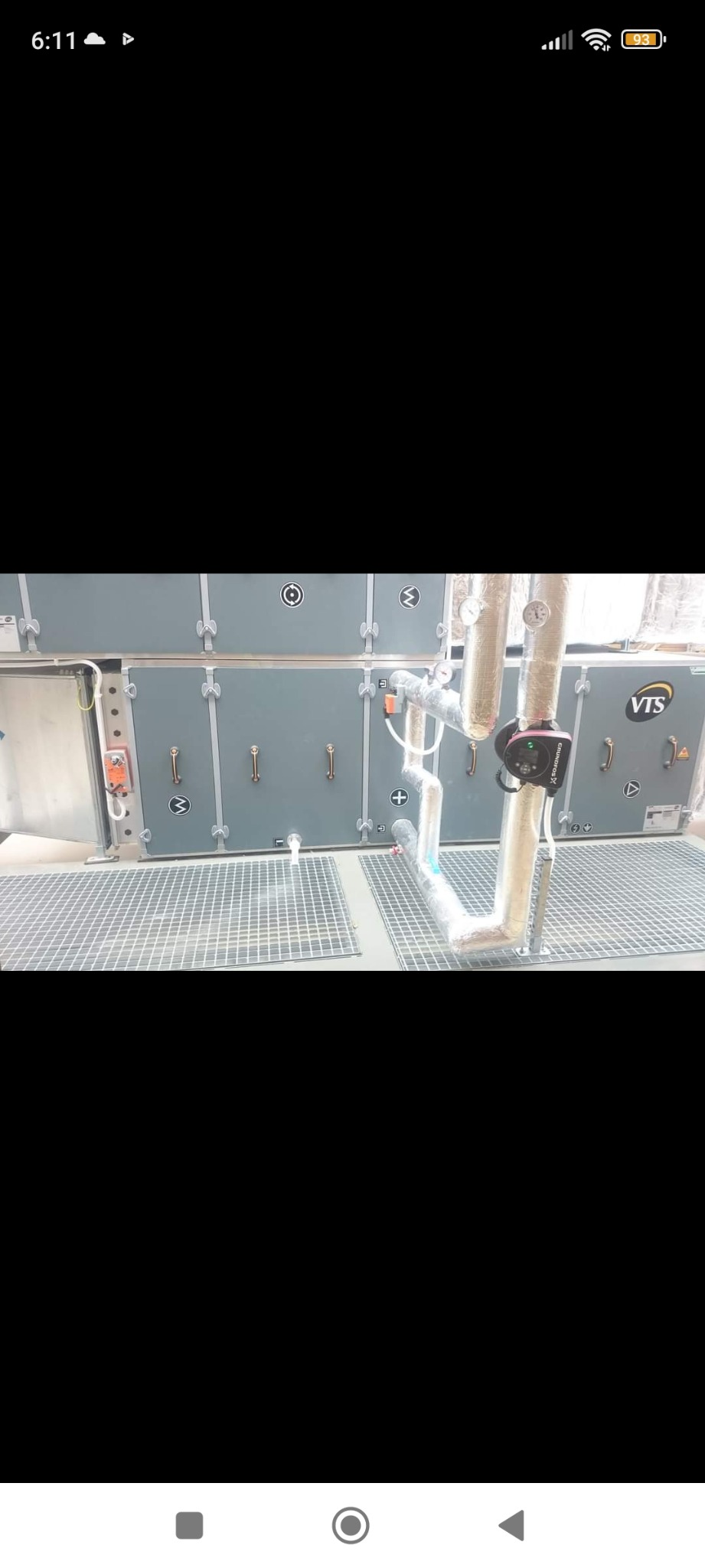 Szara centrala wentylacyjna VTS z rurami i pompą obiegową Grundfos, umieszczona na metalowej kratownicy podłogowej.