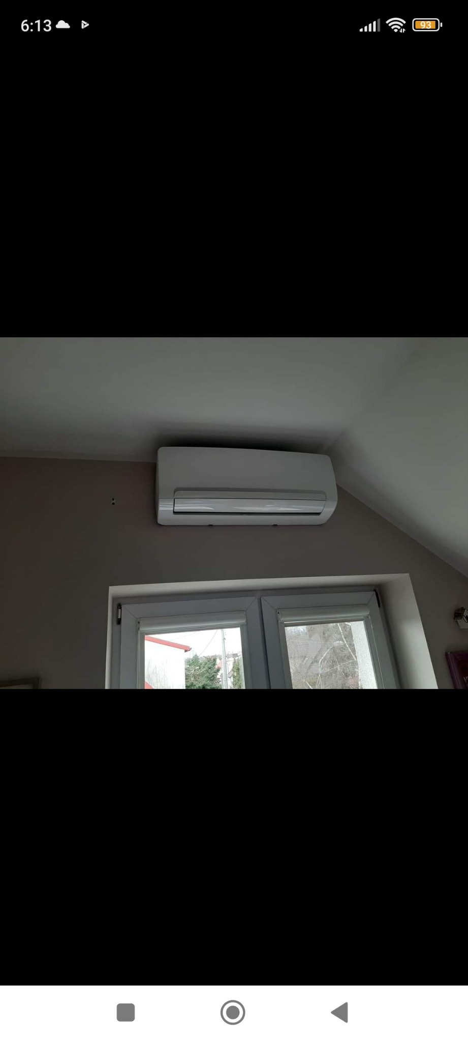 Biała klimatyzacja ścienna zamontowana nad oknem w pokoju na poddaszu, widoczne dwa otwory po wcześniejszym montażu na ścianie.