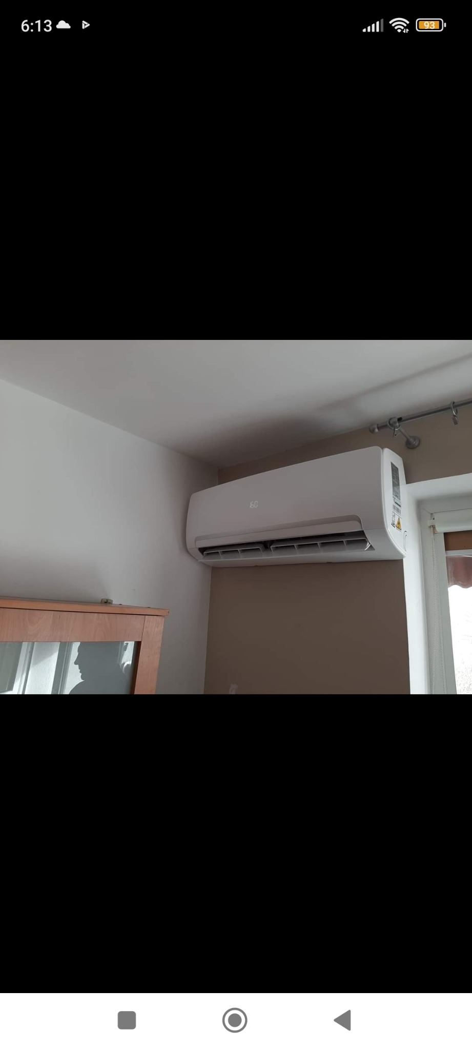 Biała jednostka klimatyzacji ściennej zamontowana w pomieszczeniu w Radzyniu Chełmińskim, widoczna nad drewnianą komodą z przeszklonymi drzwiami, obok okna z zasłoną.