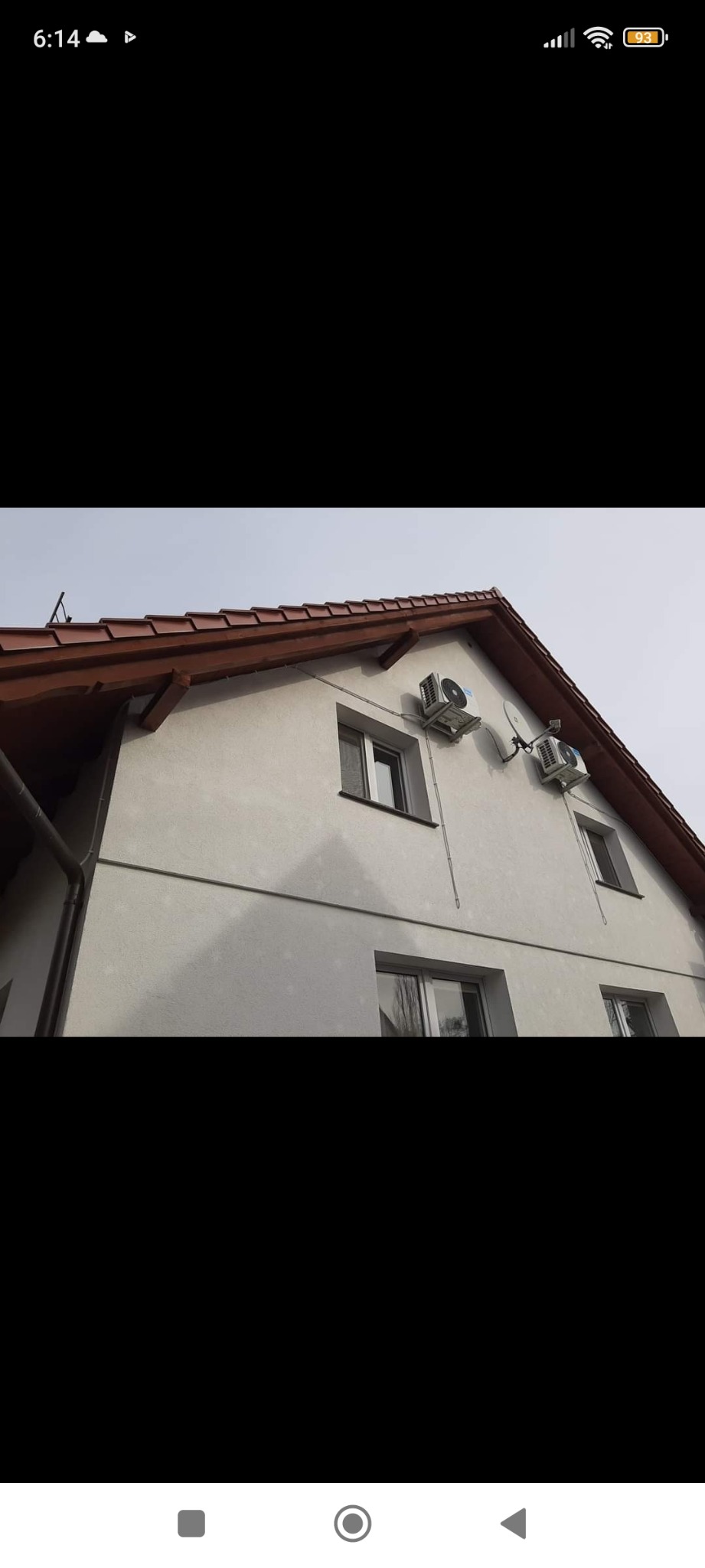 Dwa klimatyzatory zamontowane na ścianie dwupiętrowego domu z brązowym dachem, widoczne okna i instalacja elektryczna.