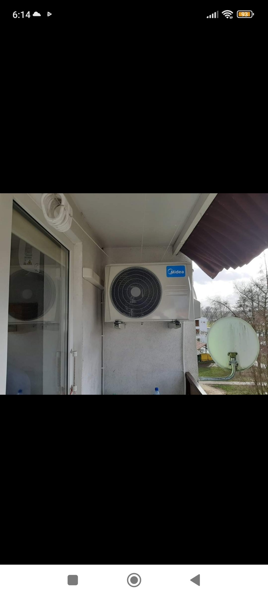 Biała jednostka zewnętrzna klimatyzatora Midea zamontowana na balkonie, widoczna antena satelitarna i kable prowadzone po ścianie.