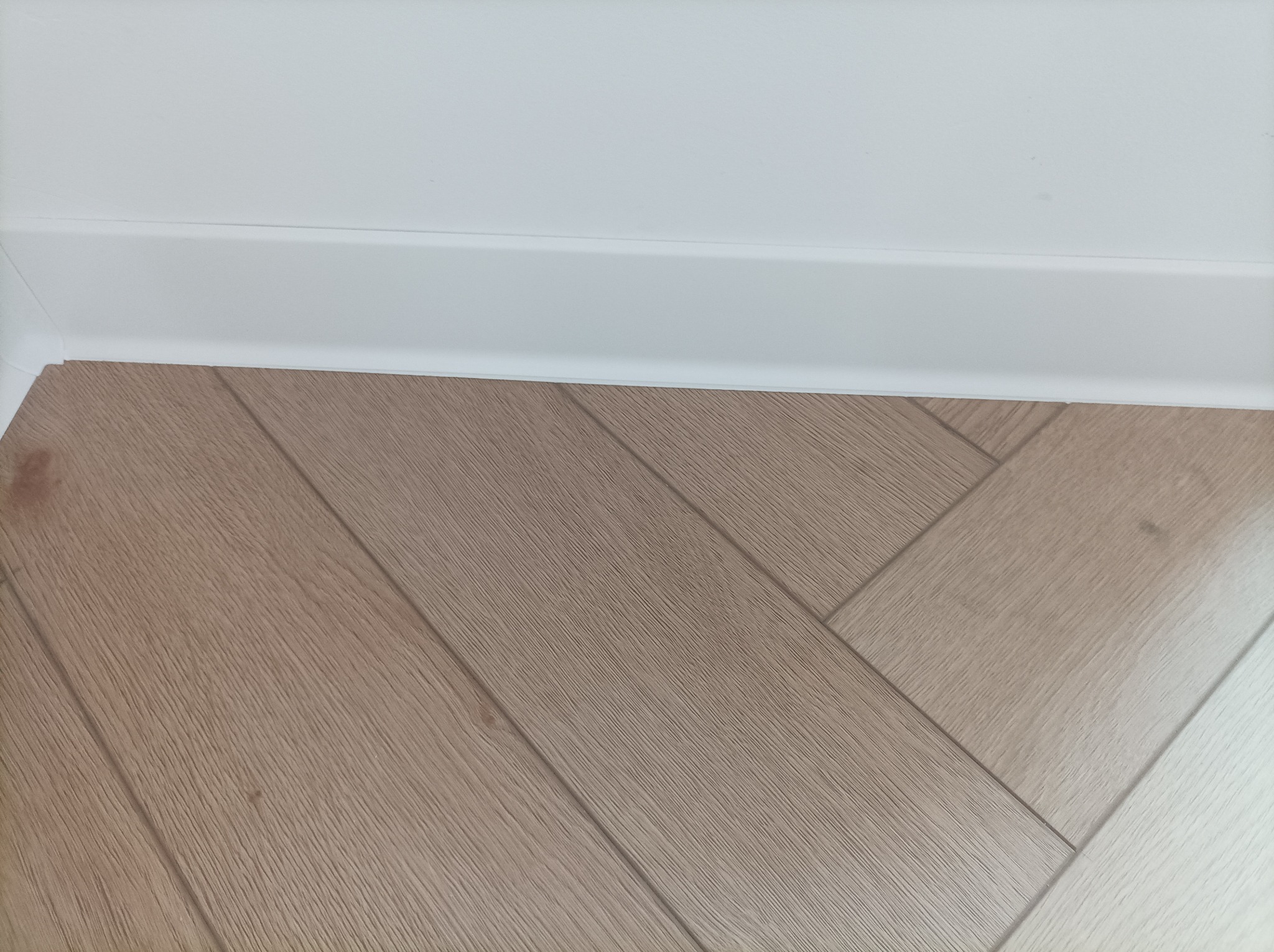 Ułożona podłoga z paneli w jodełkę, jasne drewno, biała listwa przypodłogowa i ściana.