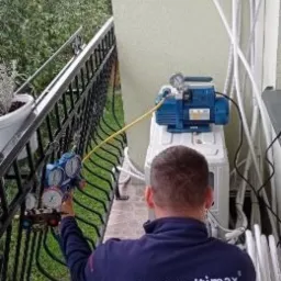 Instalator z Zamościa podłącza manometry do jednostki zewnętrznej klimatyzacji ściennej na balkonie, widoczna pompa próżniowa i rury chłodnicze.