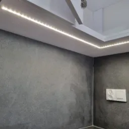 Szara ściana z gniazdkiem i włącznikiem oświetlona listwą LED w zabudowie sufitowej w Tarnowie.