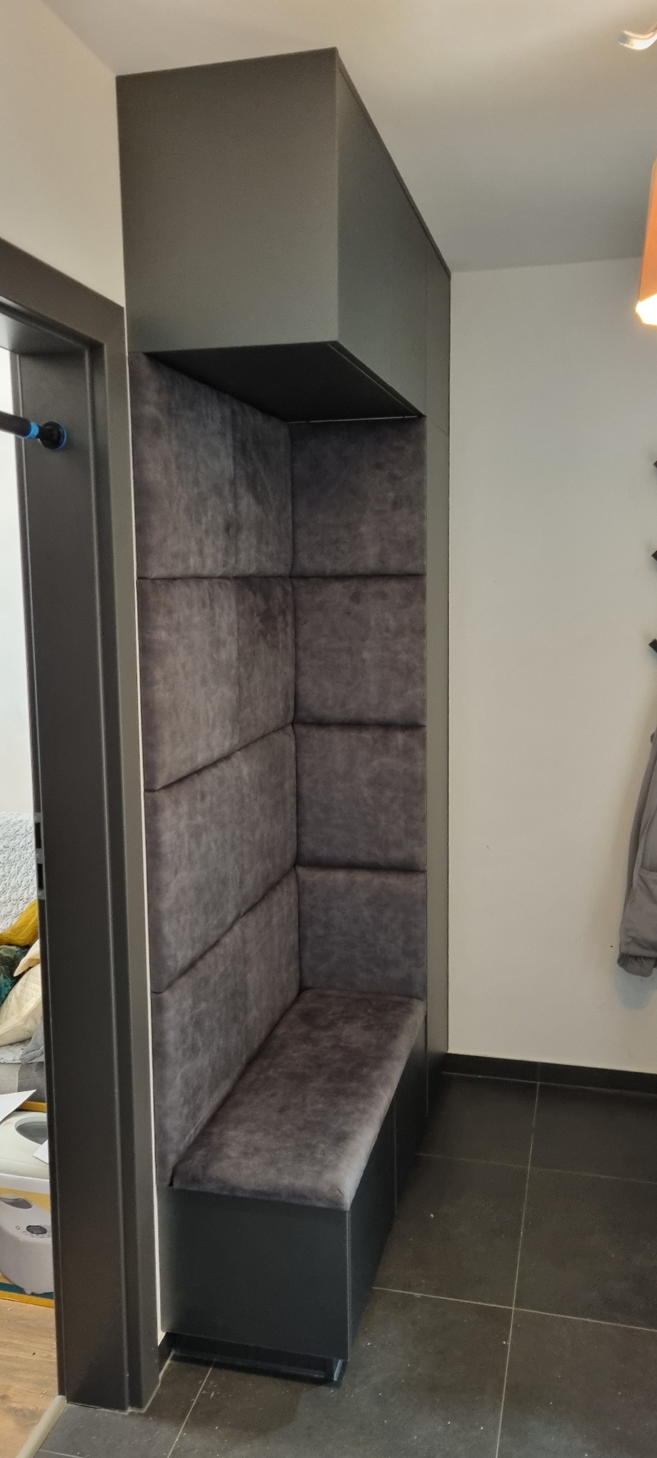 Wnęka z tapicerowanym siedziskiem i ścianami w odcieniach szarości, zabudowana szafką. Nowoczesny design, minimalistyczny styl, widok z boku, ciemna podłoga.