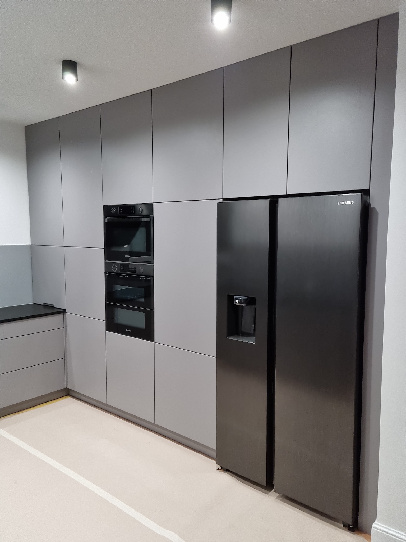 Szara zabudowa kuchenna z czarnym sprzętem AGD, w tym lodówka Samsung, w mieszkaniu w Tarnowie. Minimalistyczny design, gładkie fronty szafek.