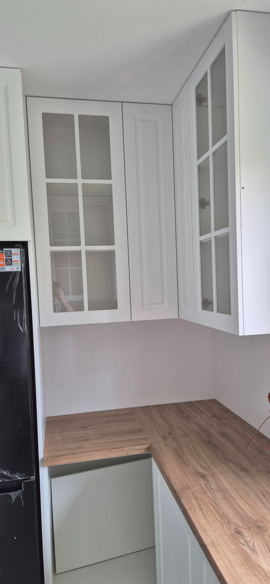 Białe szafki kuchenne z przeszklonymi frontami i drewnianym blatem, widok z bliska. Minimalistyczny design, jasne wnętrze, nowoczesne wykończenie.