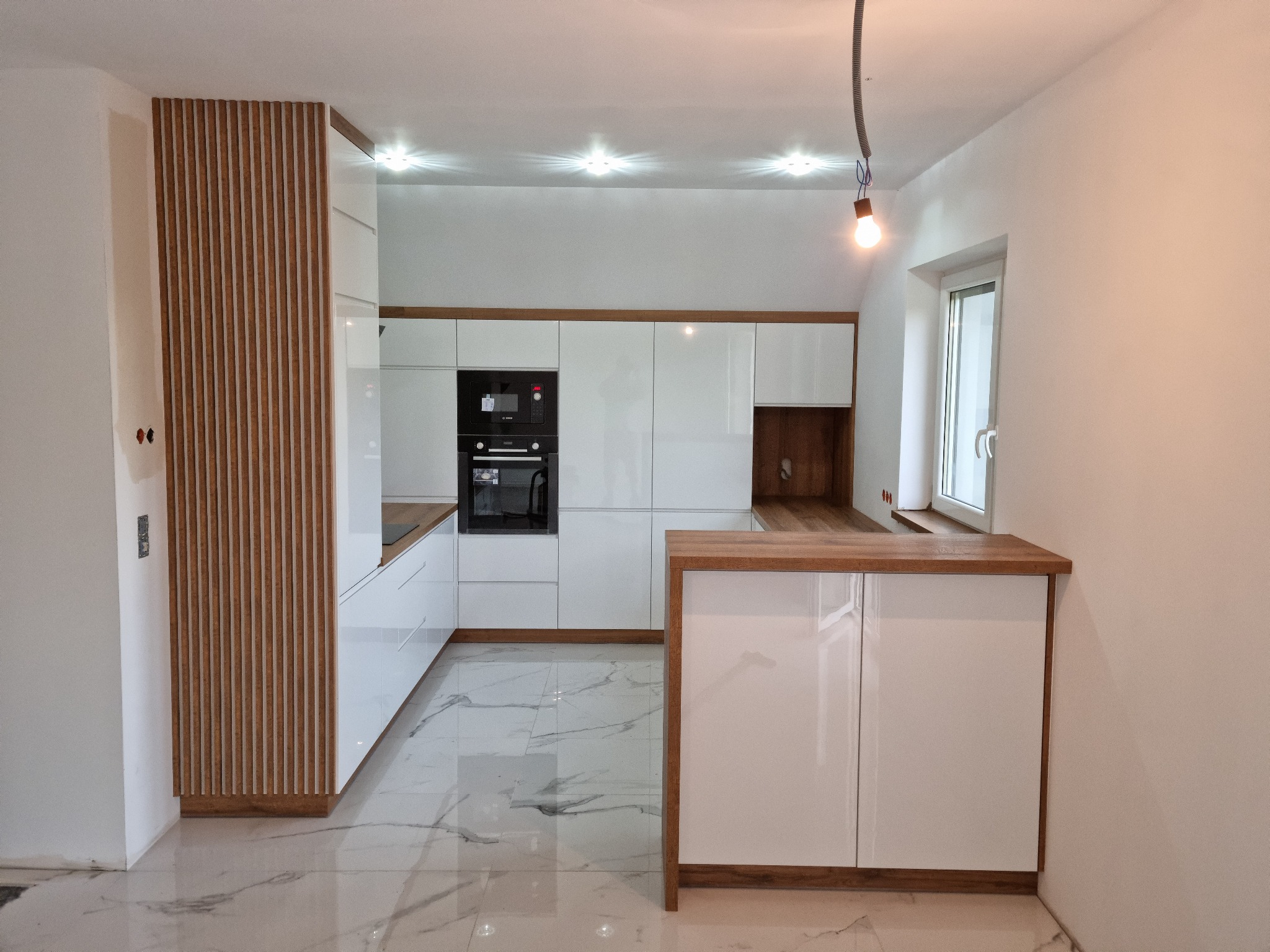 Nowoczesna biała kuchnia z drewnianymi akcentami, marmurową podłogą i wiszącą żarówką, widok z perspektywy podłogi.