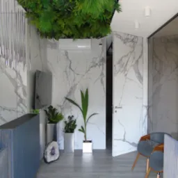 Nowoczesne wnętrze biura z marmurowymi ścianami, sztuczną roślinnością na suficie i szarymi panelami podłogowymi, uzupełnione minimalistycznymi meblami i dekoracjami.